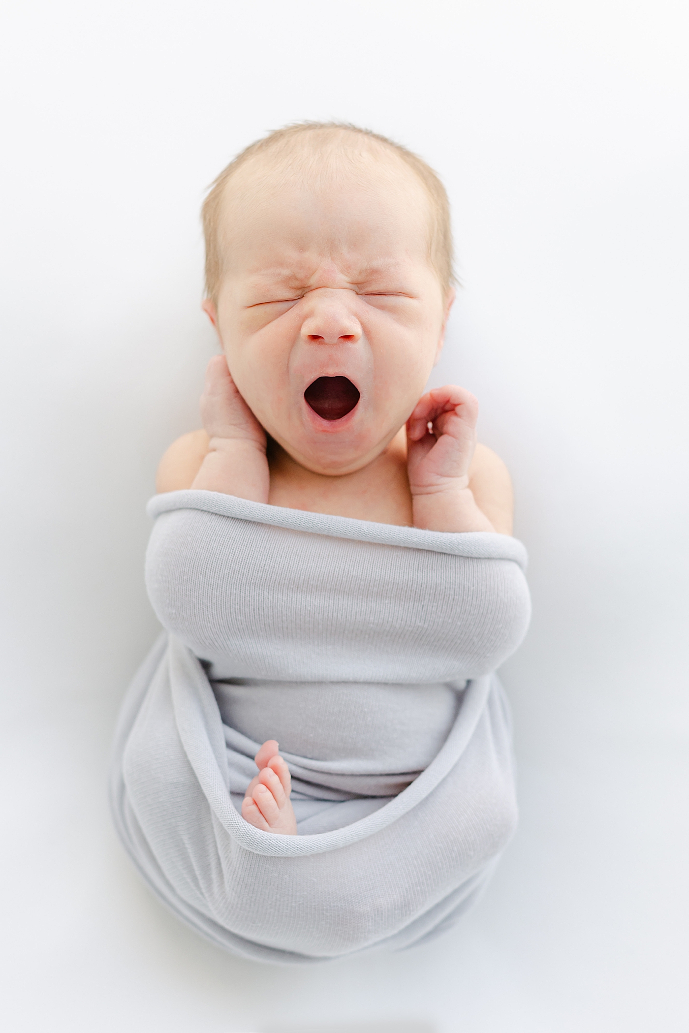 Newborn baby boy in a gray swaddle yawning | Image by Sana Ahmed Photography 
