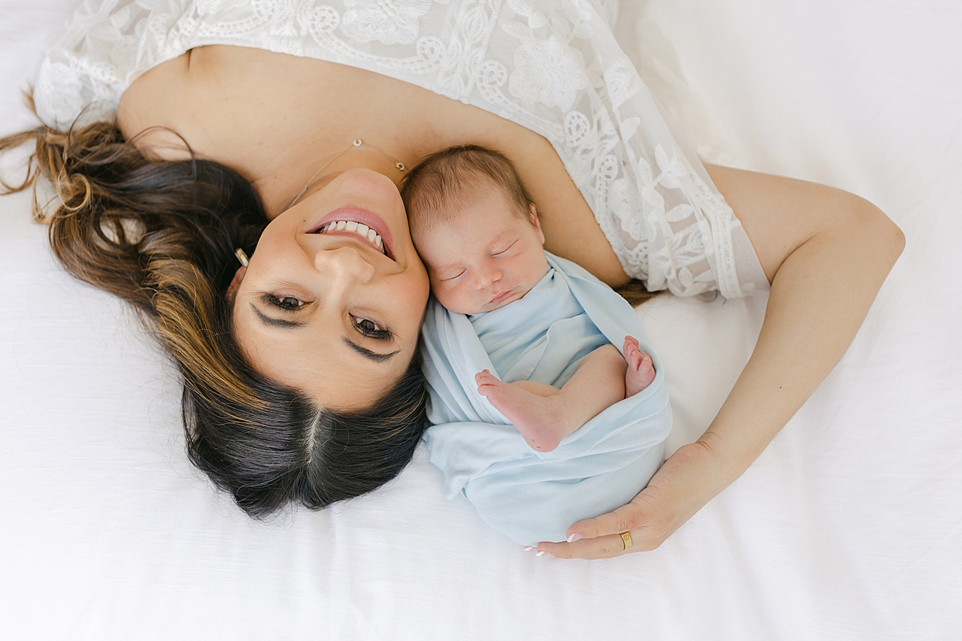Mom smiling laying on a bed with her newborn baby | Image by Sana Ahmed Photography 