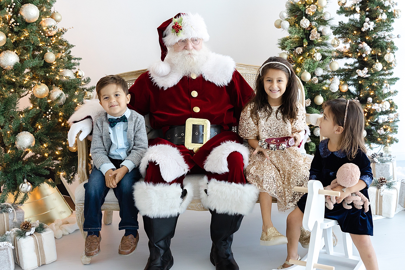 Santa sitting on a couch with three siblings during Santa mini sessions in Austin | Image by Sana Ahmed Photography