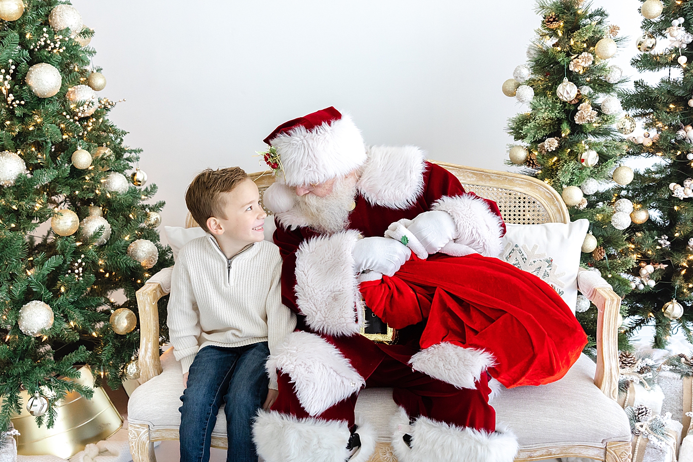 Santa sitting on a couch with a little boy in a white sweater during Santa mini sessions in Austin | Image by Sana Ahmed Photography