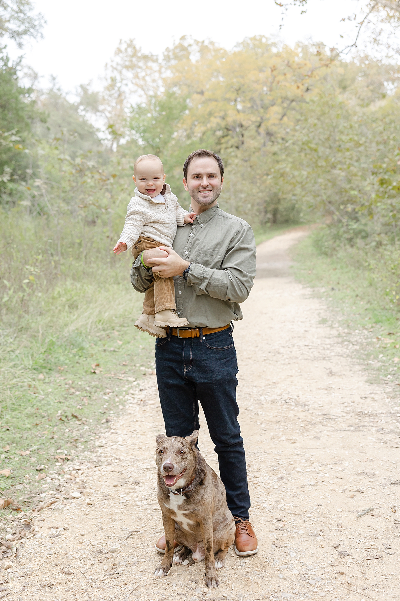 Dad holding his little boy with their dog on a dirt path | Image by Sana Ahmed Photography