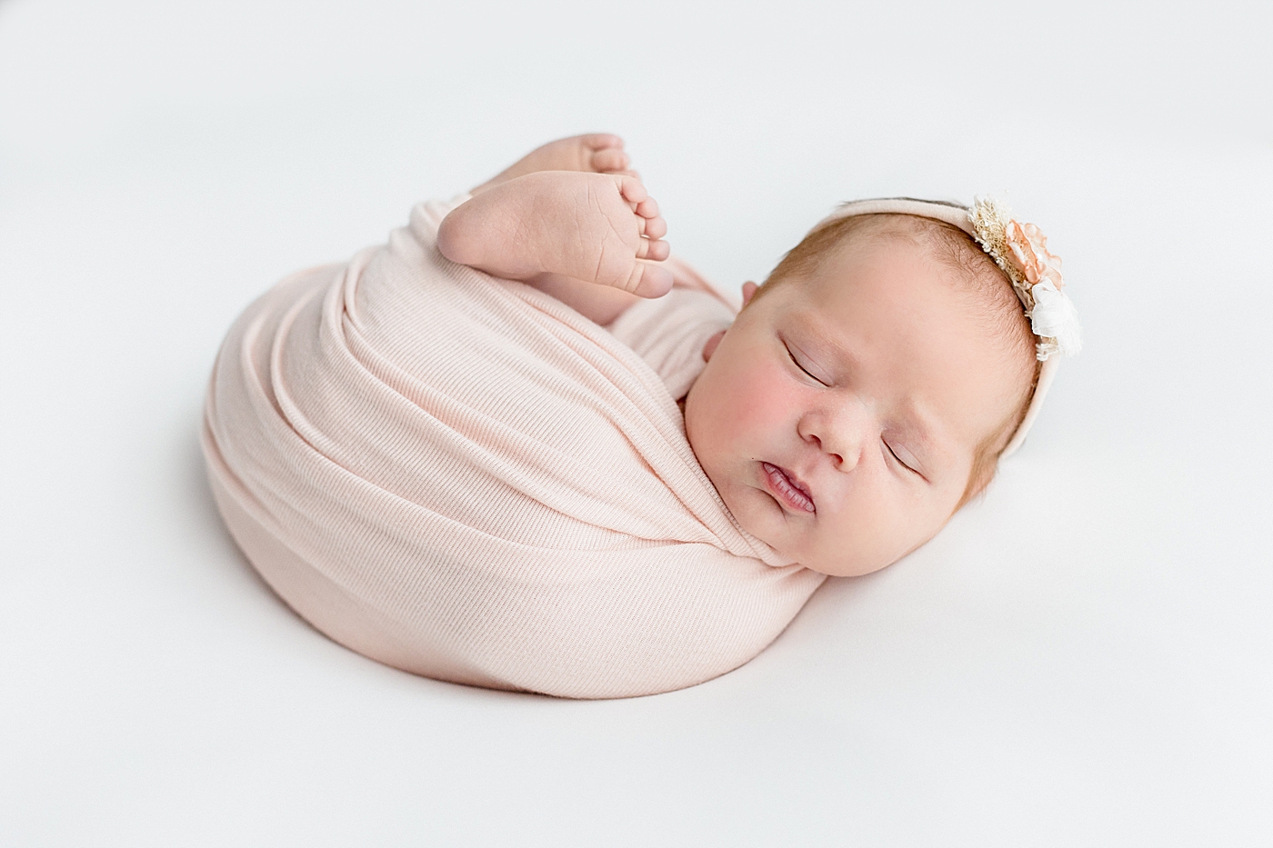 Newborn baby girl in a pink swaddle wearing a headband | Image by Sana Ahmed Photography