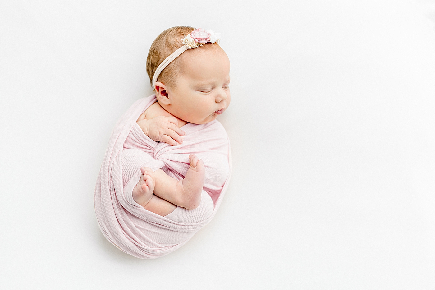 Baby girl wrapped in a pink swaddle sleeping | Image by Sana Ahmed Photography