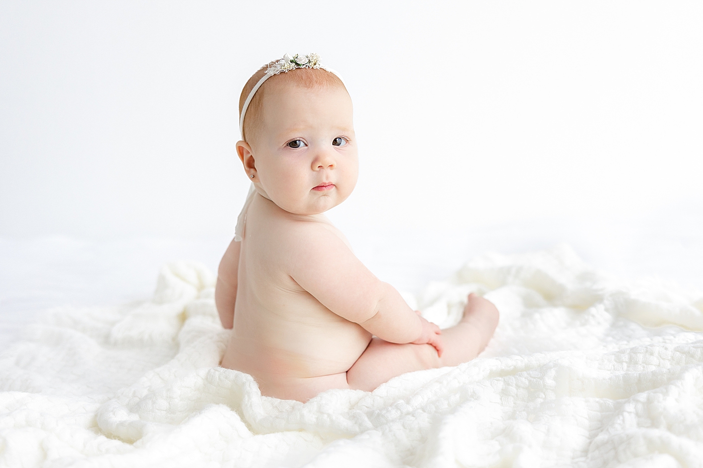 Baby girl wearing a headband sitting on a white blanket | Image by Sana Ahmed Photography