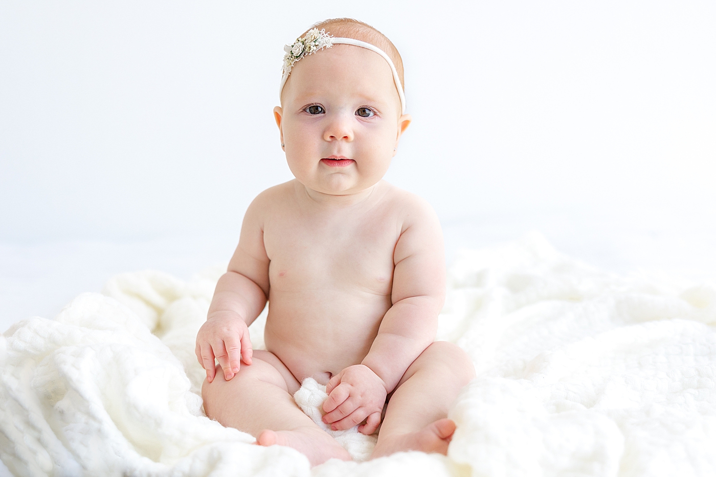 Baby girl in a headband sitting on a blanket | Image by Sana Ahmed Photography