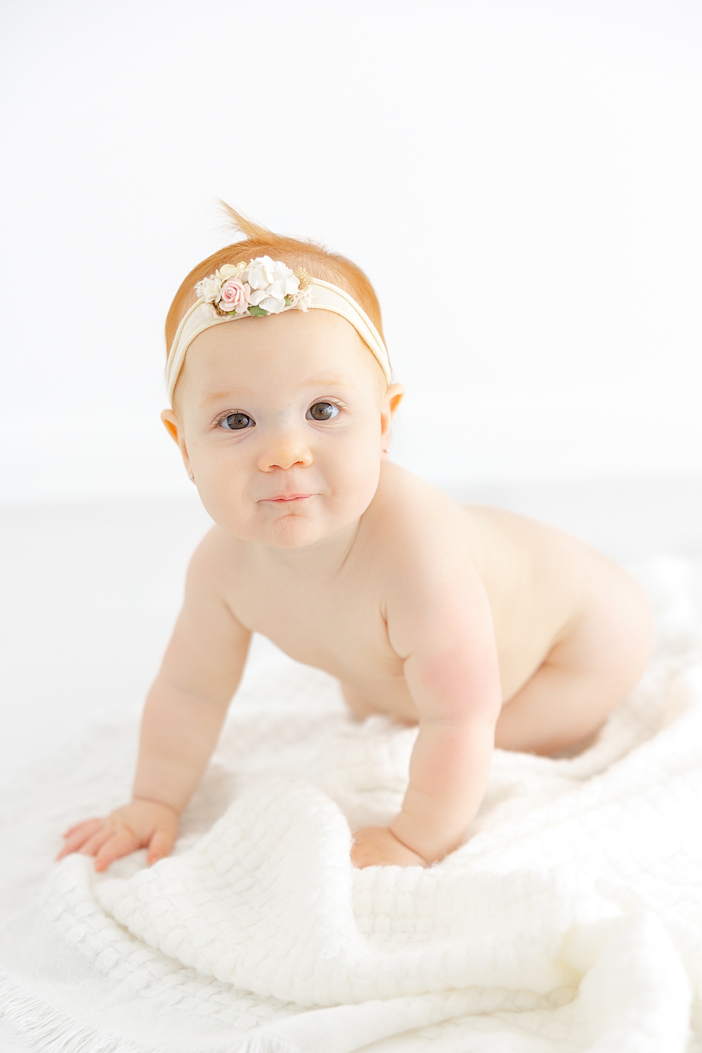 Baby girl with a floral headband on a white blanket | Image by Sana Ahmed Photography