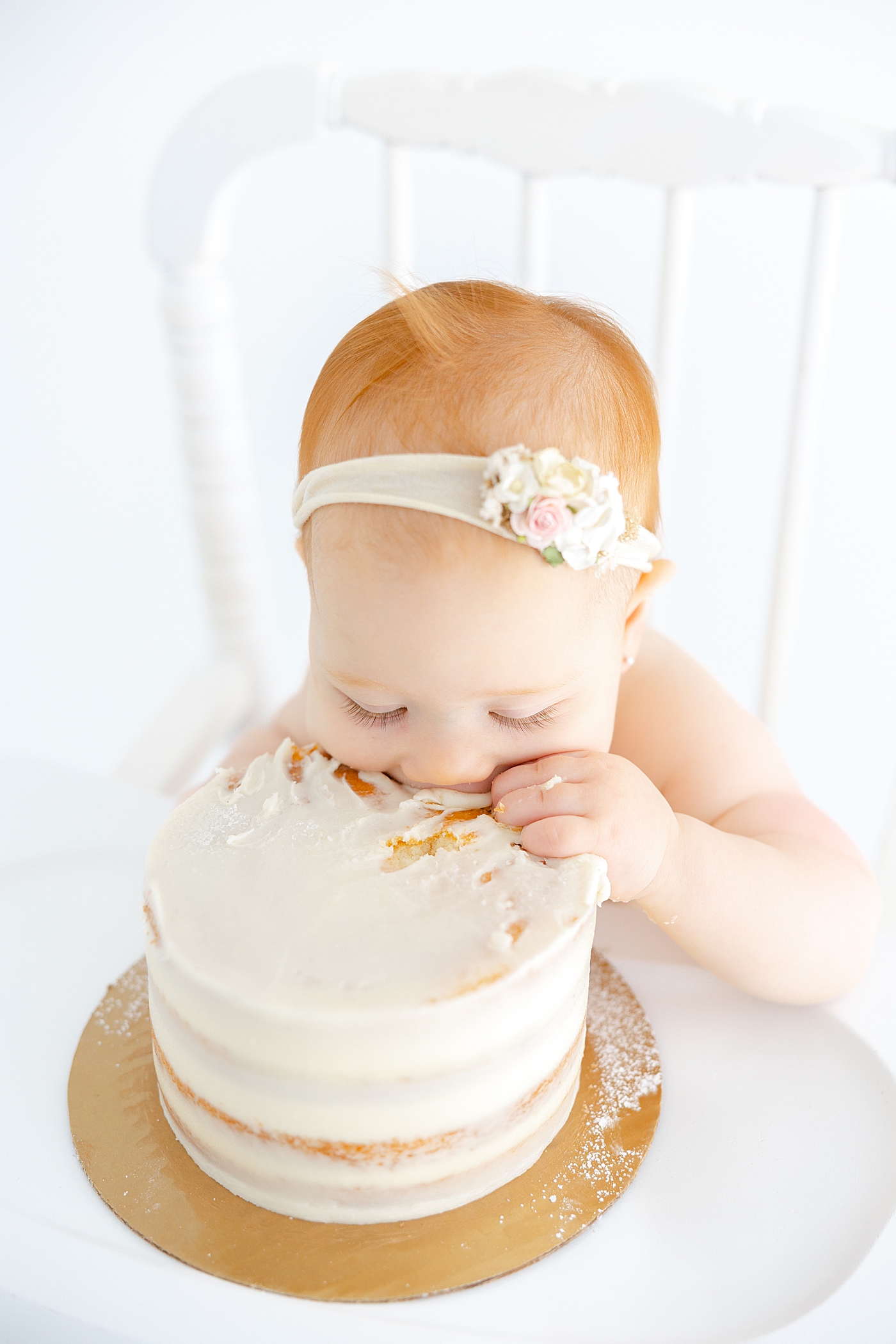 Redhead baby girl eating cake during her One Year Milestone Collection | Image by Sana Ahmed Photography