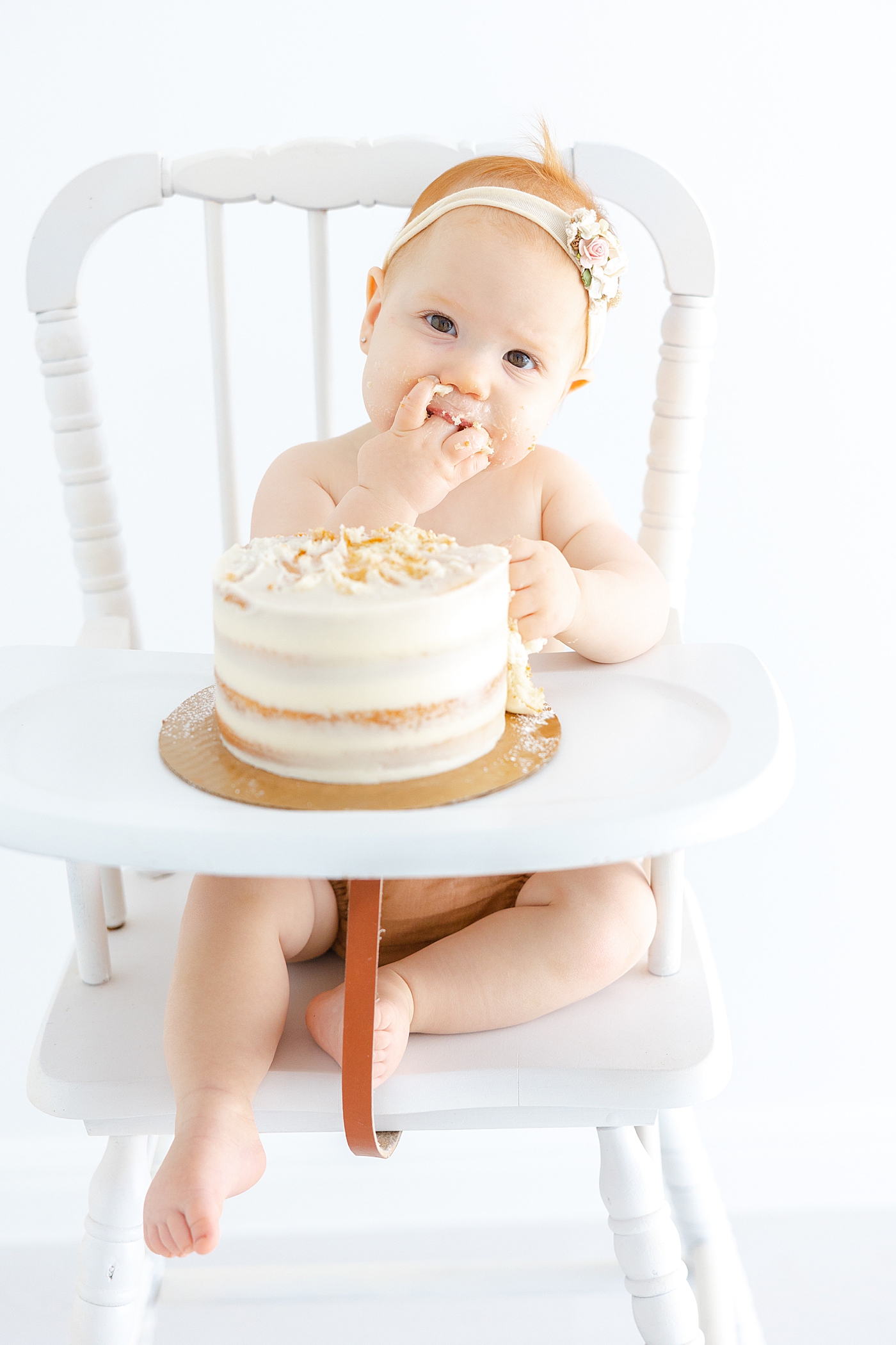 Image of baby girl in a highchair eating cake during her One Year Milestone Collection | Image by Sana Ahmed Photography