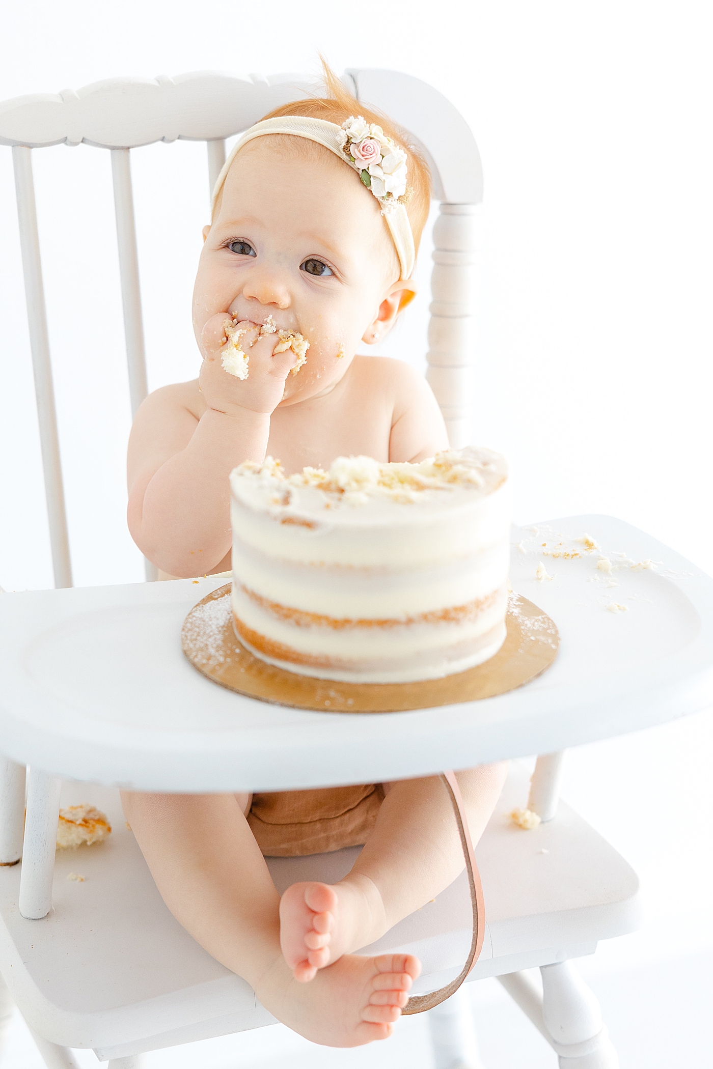 Baby girl eating her smash cake in a white highchair | Image by Sana Ahmed Photography