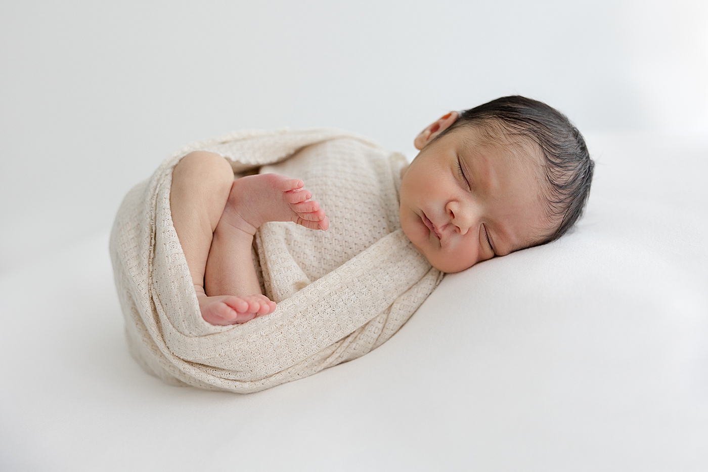 Sleeping newborn wrapped in a cream swaddle during his Studio Newborn Session in Austin | Image by Sana Ahmed Photography 