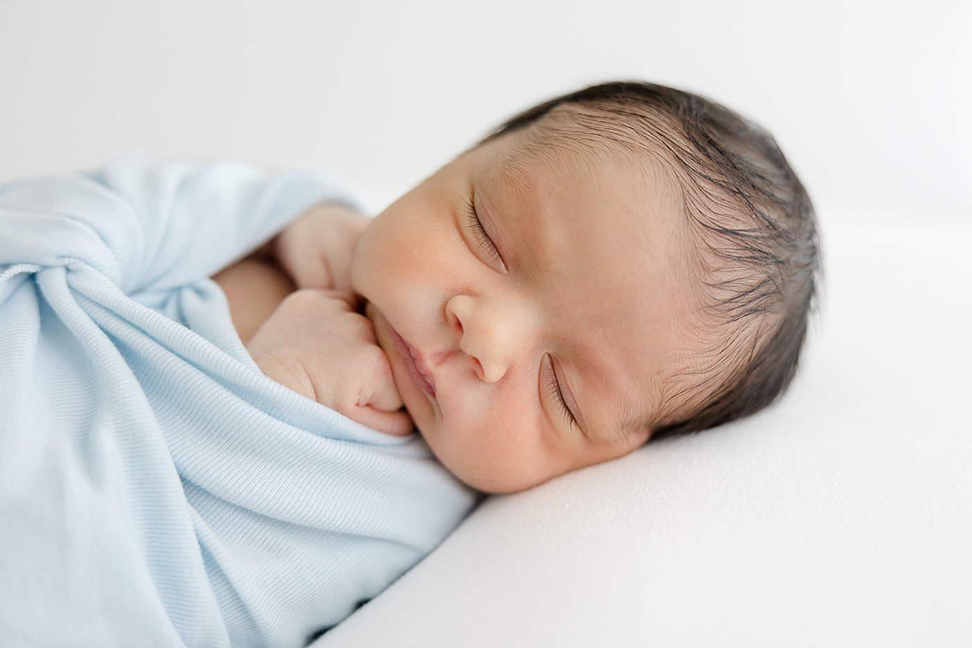 Newborn sleeping while wrapped in a light blue swaddle | Image by Sana Ahmed Photography 