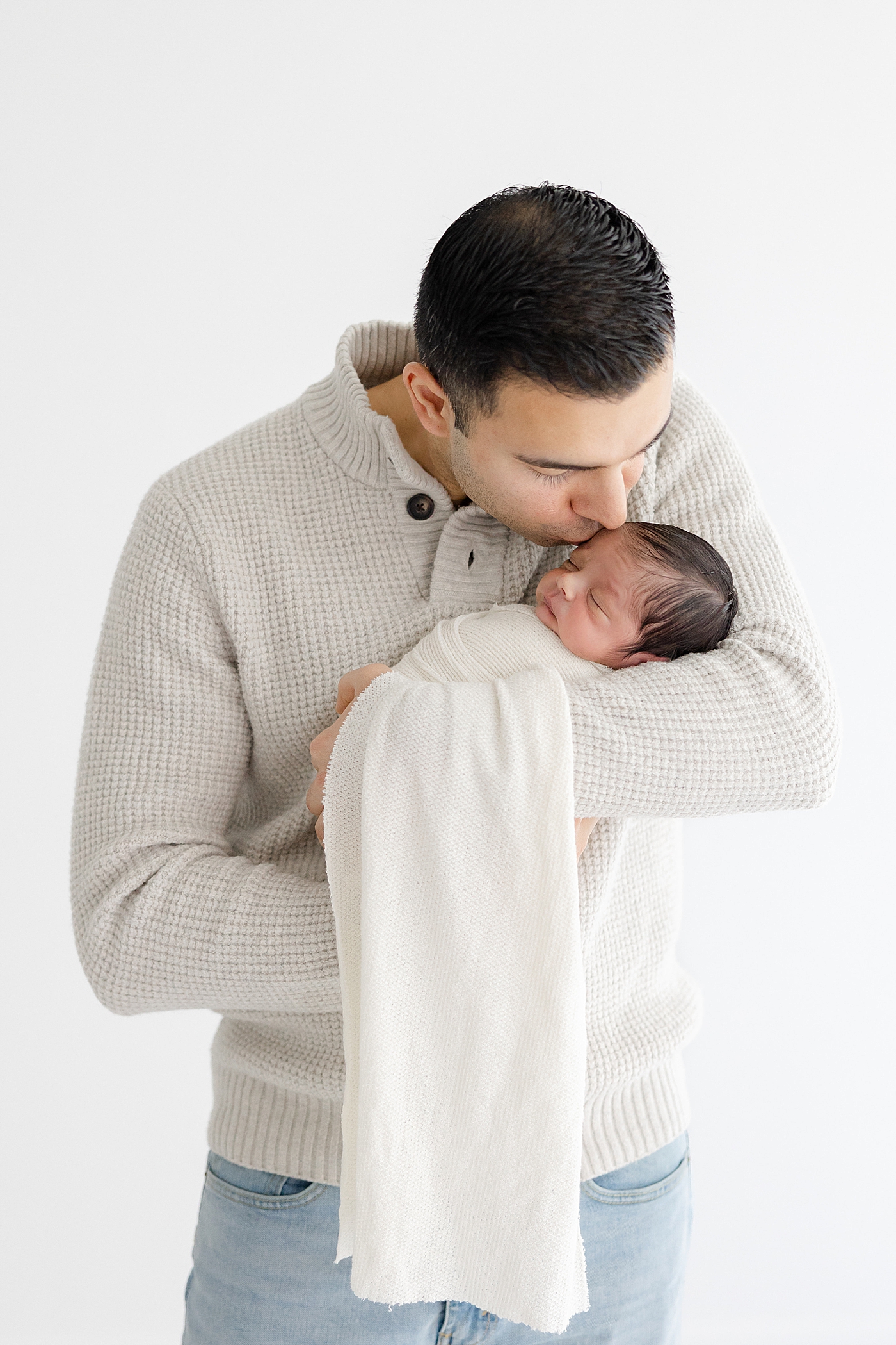 Dad kissing his sleeping baby during their Studio Newborn Session in Austin | Image by Sana Ahmed Photography 