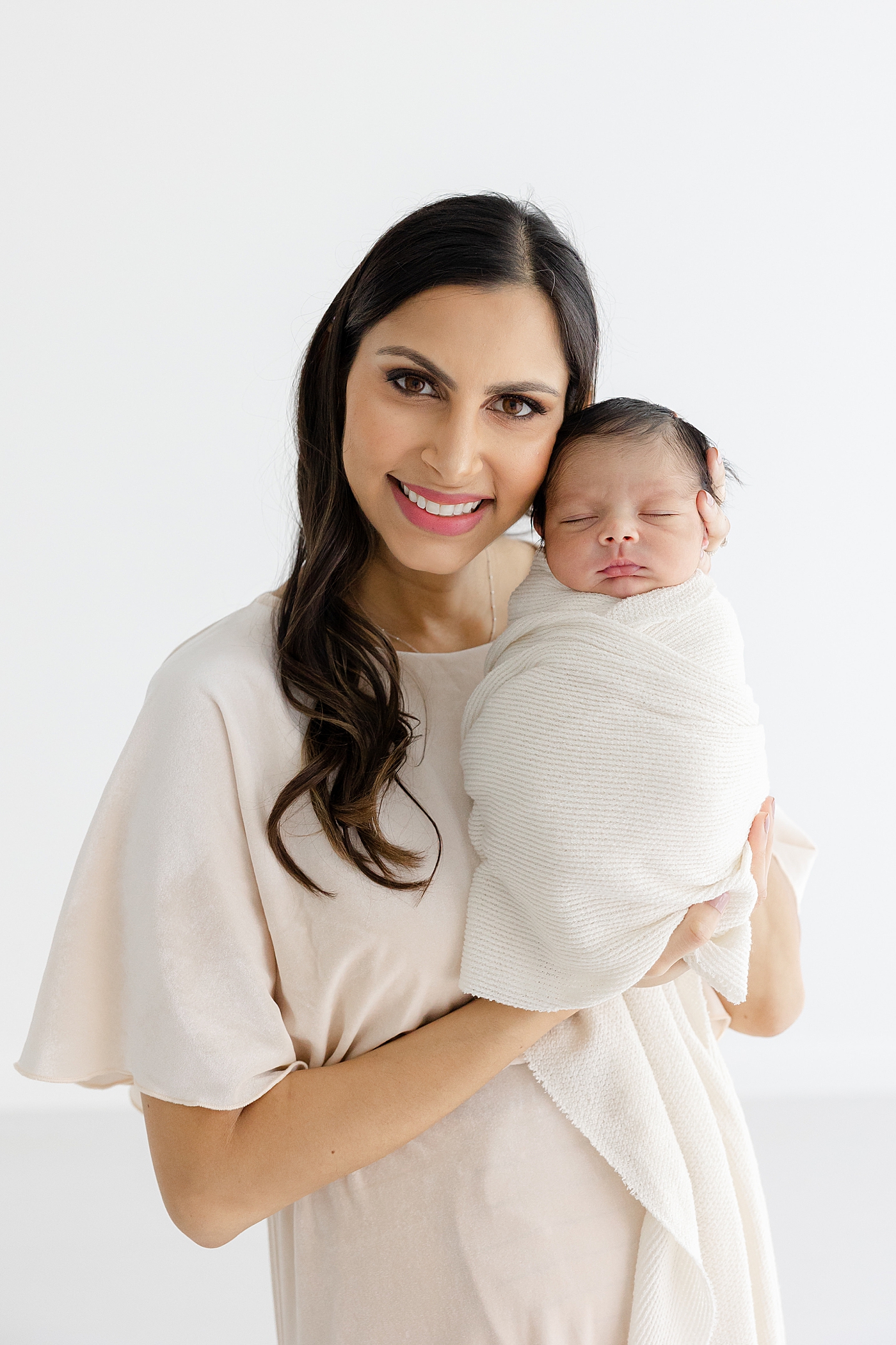 Mom smiling, holding her new baby during their Studio Newborn Session in Austin | Image by Sana Ahmed Photography 