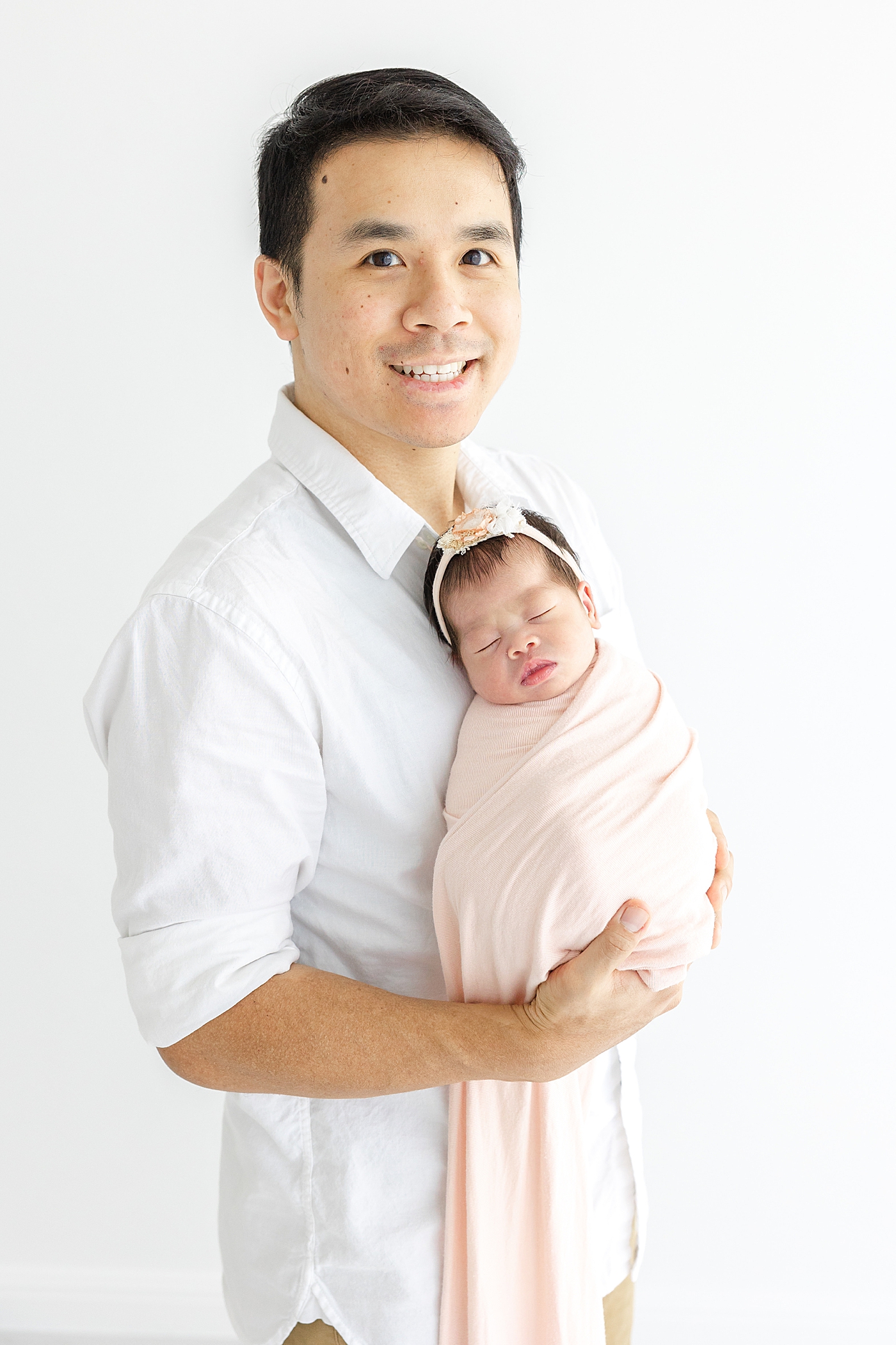 Dad smiling holding his new baby during her Newborn sessions with siblings | Image by Sana Ahmed
